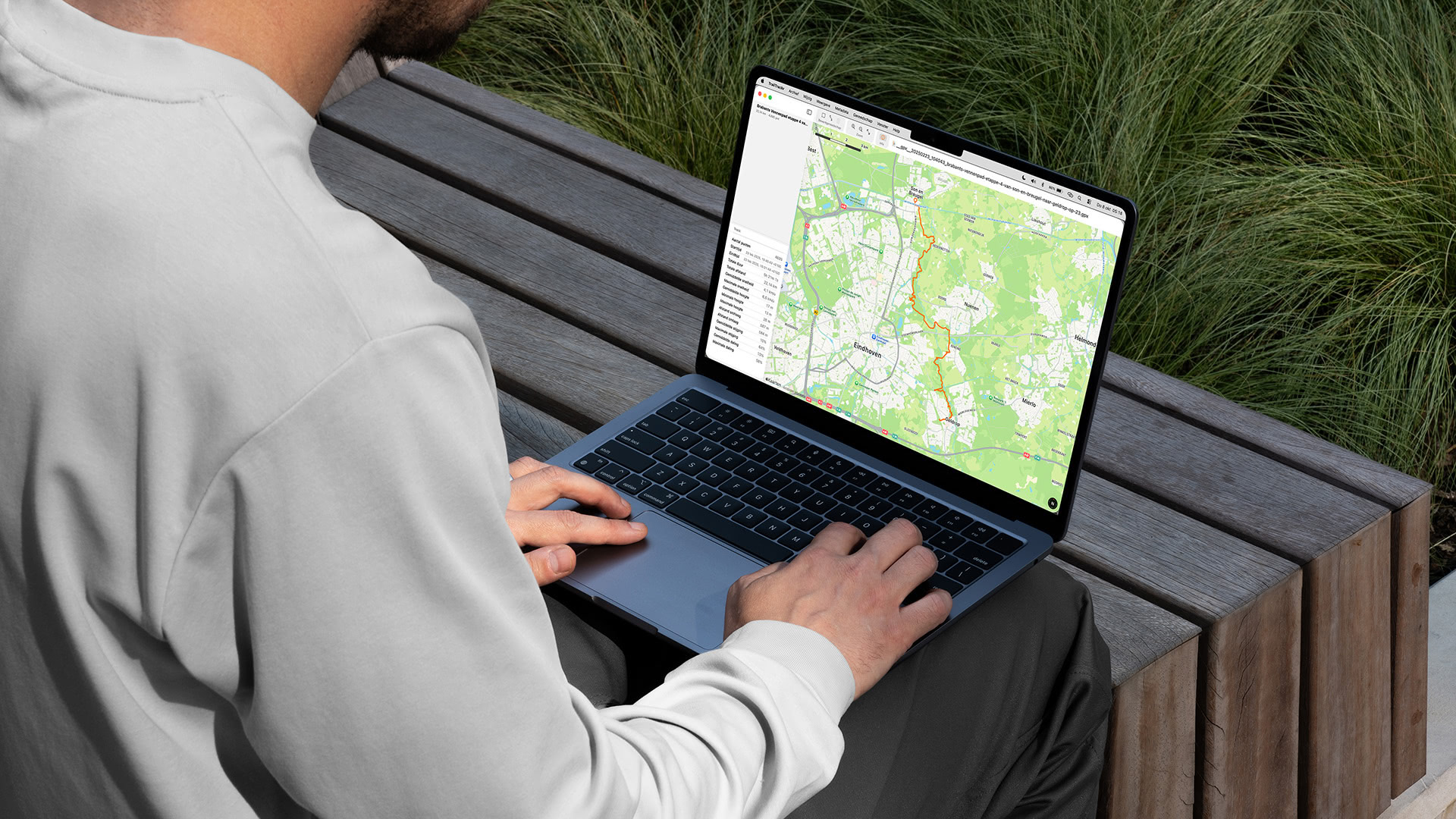 Persoon op een bankje met een MacBook waarop TrailTrackr voor Mac een wandelroute op de kaart toont