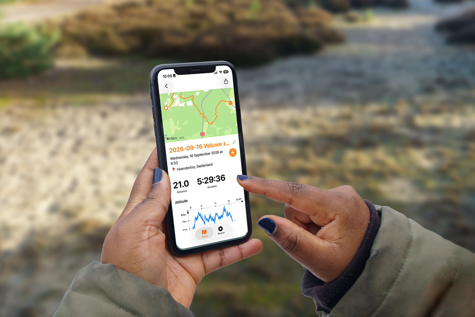 Twee handen met een iPhone die een voltooide hike toont met routekaart, afstand, duur en hoogtegrafiek