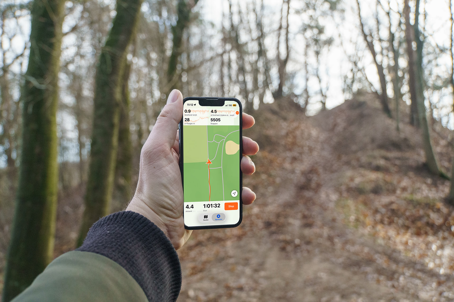 Hand met een iPhone die een hike in een bos opneemt, met live statistieken en de route op een kaart